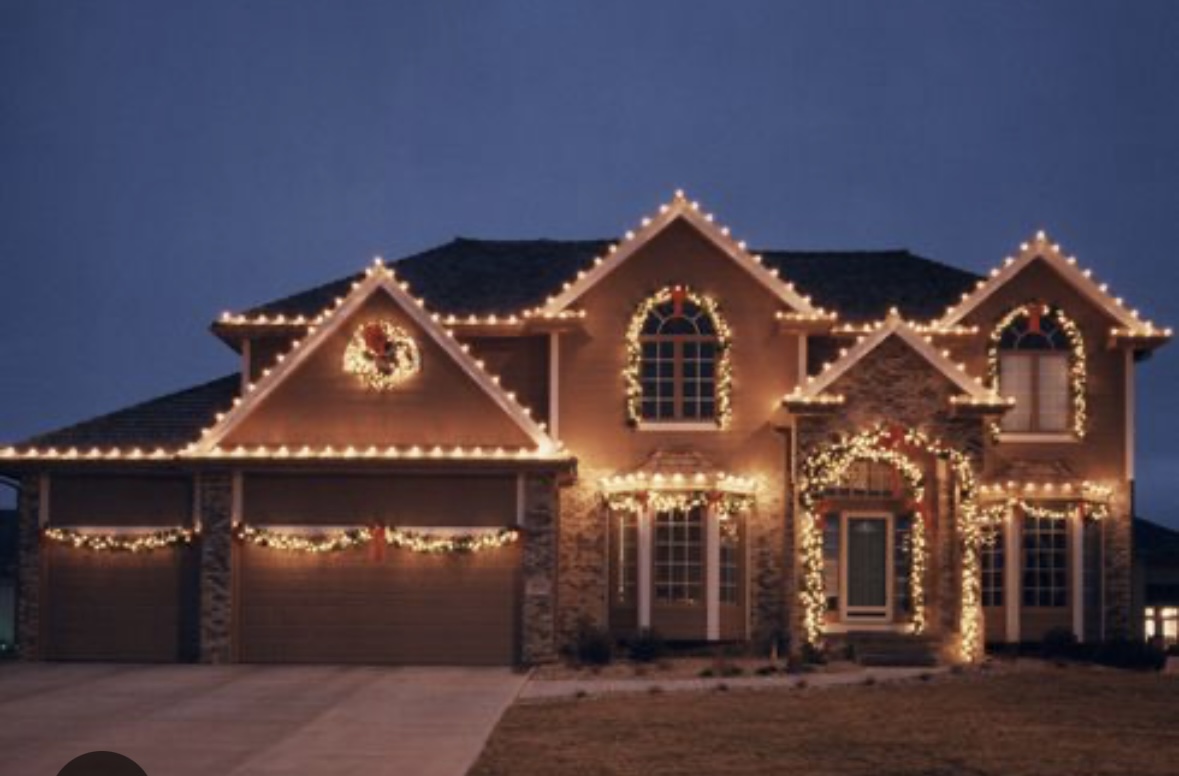Warm white C9 roofline with garland-wrapped columns and doorway on a stone-and-brick home