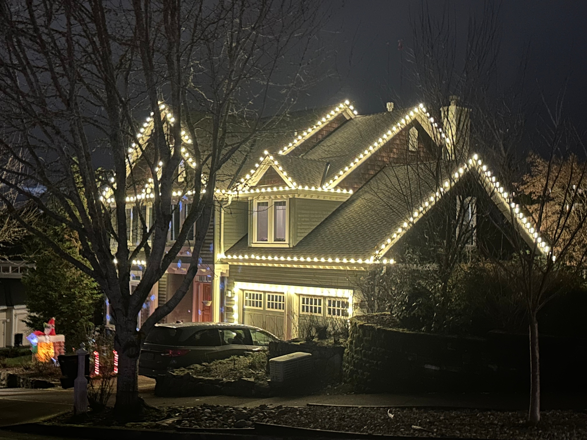 Warm white C9 roofline outlining a craftsman home with wrapped tree at night